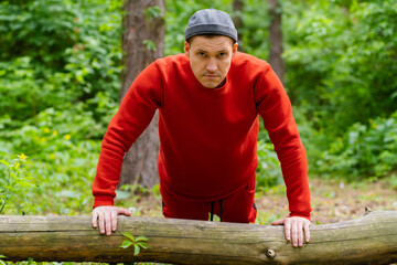 A man performs push-ups using the log as support. The backdrop is a dense forest with trees and foliage.
