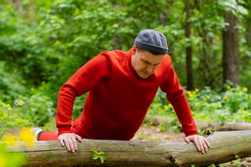A man performs push-ups using the log as support. The backdrop is a dense forest with trees and foliage.