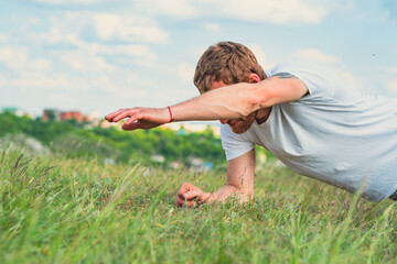A focused man performs push-ups on a grassy field during early morning hours
