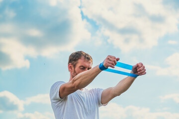 A professional sportsman in a white shirt is holding a Elastic band expander. He appears focused and determined as he prepares his shoulder and arm muscles for the workout ahead.
