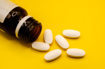 White Tablets Spilled from Medicine Bottle on Bright Yellow Background