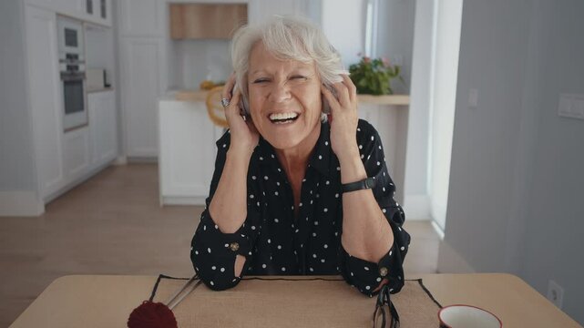 Beautiful senior old woman with gray hair at home - Youthful elderly granmother spending quality time at home. Listening to music with the headphones.