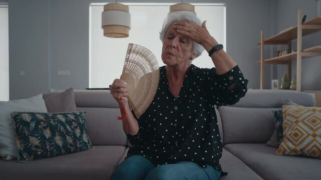 Beautiful senior old woman with gray hair at home - Using the fan against the high summer heat.