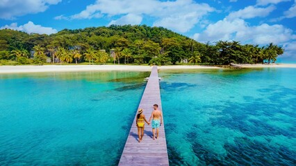 A joyful couple explores the serene wooden boardwalk leading to crystal-clear waters on Koh Kham island, Thailand. The tropical scenery and vibrant colors create a perfect vacation atmosphere.