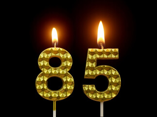 Burning golden birthday candles isolated on black background, number 85.	
