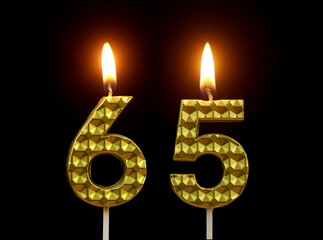 Burning golden birthday candles isolated on black background, number 65.	