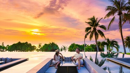 A man and woman relax together in a stunning infinity pool, gazing at a vibrant sunset over the...