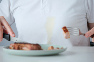 Spilled tough grease stain on white clothes. A person siting at a dining table preparing to eating juicy steak on a plate. Concept of daily stains on clothes