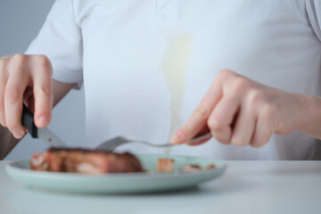 Spilled tough grease stain on white clothes. A person siting at a dining table preparing to eating...
