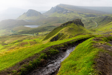 Obraz premium The Quiraing, Isle of Skye lush green landscapes, pure air, dramatic cliffs. A surreal trail through wild nature, perfect for trekking, silence, breathing untouched beauty, mystical rock formations.
