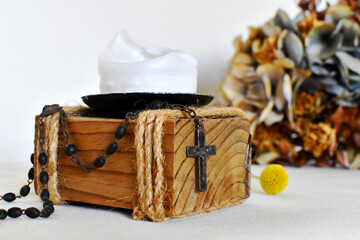 Dark rosary for prayers on a light background, yellow dried flower and wooden candlestick with white candle