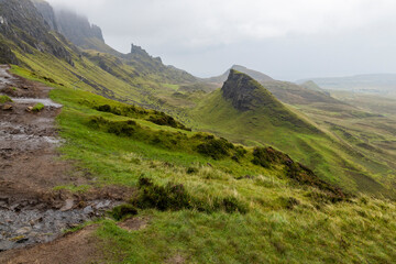Fototapeta premium The Quiraing, Isle of Skye lush green landscapes, pure air, dramatic cliffs. A surreal trail through wild nature, perfect for trekking, silence, breathing untouched beauty, mystical rock formations.