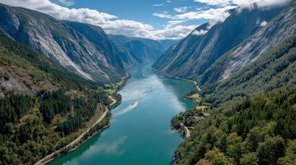 Aerial view of a river flowing through a mountain valley, surrounded by lush green forests and rocky cliffs under a partly cloudy sky.