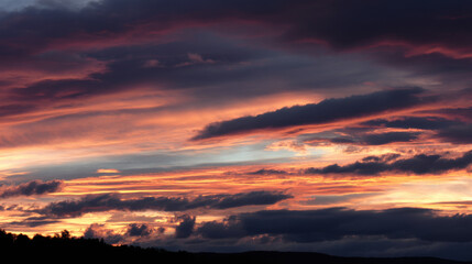 Fototapeta premium Fiery shades of orange and purple paint the dramatic sky as the sun sets behind the distant silhouetted hills, creating a breathtaking and unforgettable view.