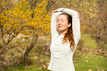 Young woman stretching arms up, doing breathing exercise and morning yoga practice, meditating in...