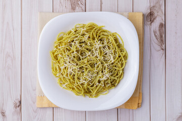 Italian pasta spaghetti on a plate with pesto sauce and parmesan cheese