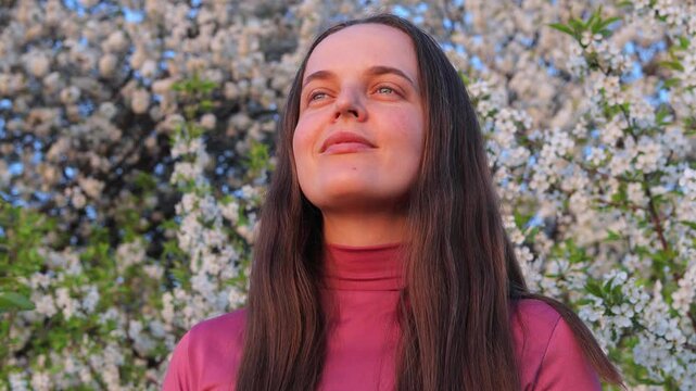 Woman with long hair breathes freely and smiles amidst blooming flowers in spring, experiencing allergies due to the abundant pollen surrounding her