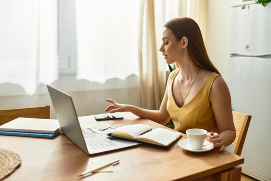 Young beautiful woman engaging in focused work while enjoying a warm beverage at home