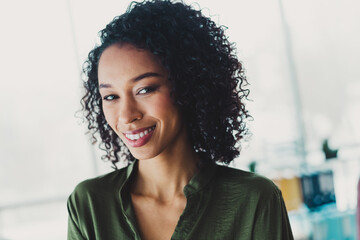 Confident young businesswoman with curly hair smiling confidently in a bright modern office...