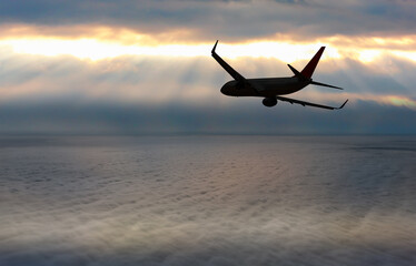 Silhouette of airplane flying over amazing clouds at sunset
