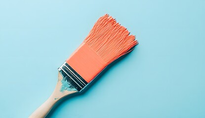 Paintbrush with coral-colored paint on a pastel blue background, flat lay.