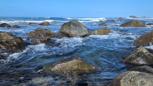 Large beautiful stones in the waves surf on Benijo beach, Canary Islands. Atlantic Ocean. Blue sunny sky with clouds. Benijo beach, Anaga Rural Park, municipality of Santa Cruz de Tenerife. Spain.
