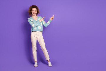 Smiling young woman pointing to the side on a purple background wearing a floral cardigan Casual and whimsical fashion concept