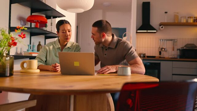 Tense emotional interaction between couple during video conference. Capturing stressful communication dynamics while seated at kitchen table with visible interpersonal tension and unresolved conflict