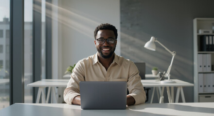 Bright and productive Black businessman working on laptop in sunlit office. Young African American man office worker in modern workplace. Positive work environment, technology user.