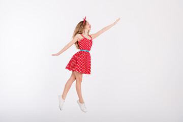 Energetic young woman in a vintage polka dot dress dancing gracefully with joy on a white background