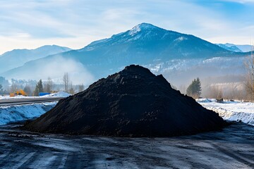 Black powder pile of coal on a construction site background. A pile of black soil on a mountain in the winter time. 