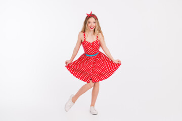 Smiling young woman dressed in a vintage red polka dot dress posing charmingly on a white...