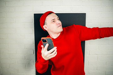 A man in a red hoodie and hat dances against a white brick wall