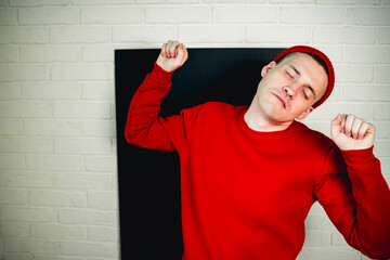A man in a red hoodie and hat dances against a white brick wall
