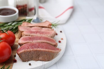 Delicious sliced beef tenderloin with different degrees of doneness, tomatoes and spices on light tiled table, closeup. Space for text