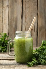 Healthy parsley smoothie in mason jar and leaves on wooden table, closeup