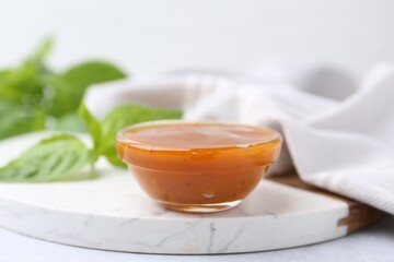 Tasty curry sauce in glass bowl and basil on white table, closeup