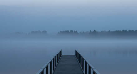 Obraz premium Wooden pier jetty extending into calm water with dense fog mist.