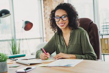 Young professional woman working at office desk with confidence and cheerfulness, wearing casual...