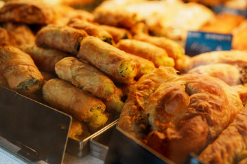 Golden brown savory pastries filled with potatoes and spinach are neatly arranged on a bakery counter, tempting customers with their appetizing aroma and flaky crusts