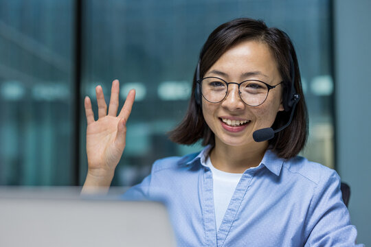 Joyful successful woman with headset close up, waving hand greeting client online remotely. Support service worker using laptop for online communication.