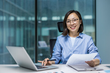 Portrait of young successful businesswoman financier at workplace inside office. Asian woman behind...