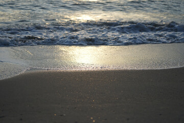 Reflection of sunlight on the wet beach with motion blurred wave surfing into the coast in background