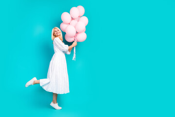 Elderly woman in white dress holding pink balloons on teal background embodying vibrant charm and cheerful enjoyment