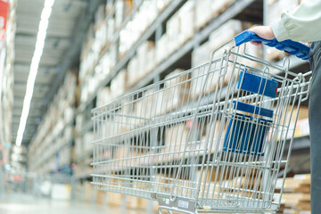 female warehouse manager pushes shopping cart through large storage area, managing shipping orders...