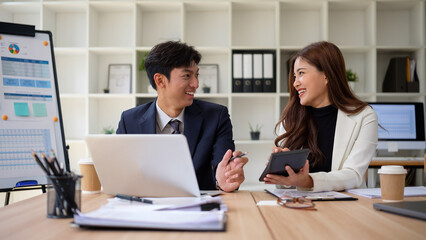 Two businesspeople discussing project with documents and laptop at modern workplace.