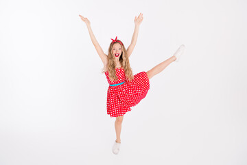 Energetic young woman in a red retro style polka dot dress leaping joyfully against a white background