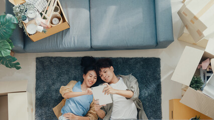 Top view. Happy Asian couple lay down on carpet use tablet shopping online furniture from decoration store in living room at new house. Husband wife move house, Apartment Rent And Ownership Concept. © tirachard