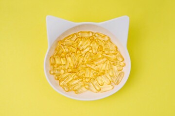 High angle view of  feeding dish fillled with fish oil omega 3 pills on yellow background. 