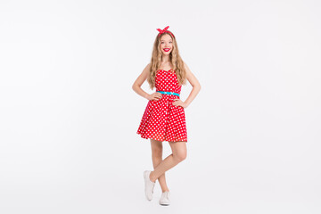 Retro styled woman in red polka dot dress striking a charming pose against a white background,...